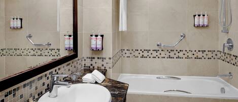 A bathroom with a bathtub, a sink, and a mirror. There are towels hanging on a rack and toiletries on the wall.