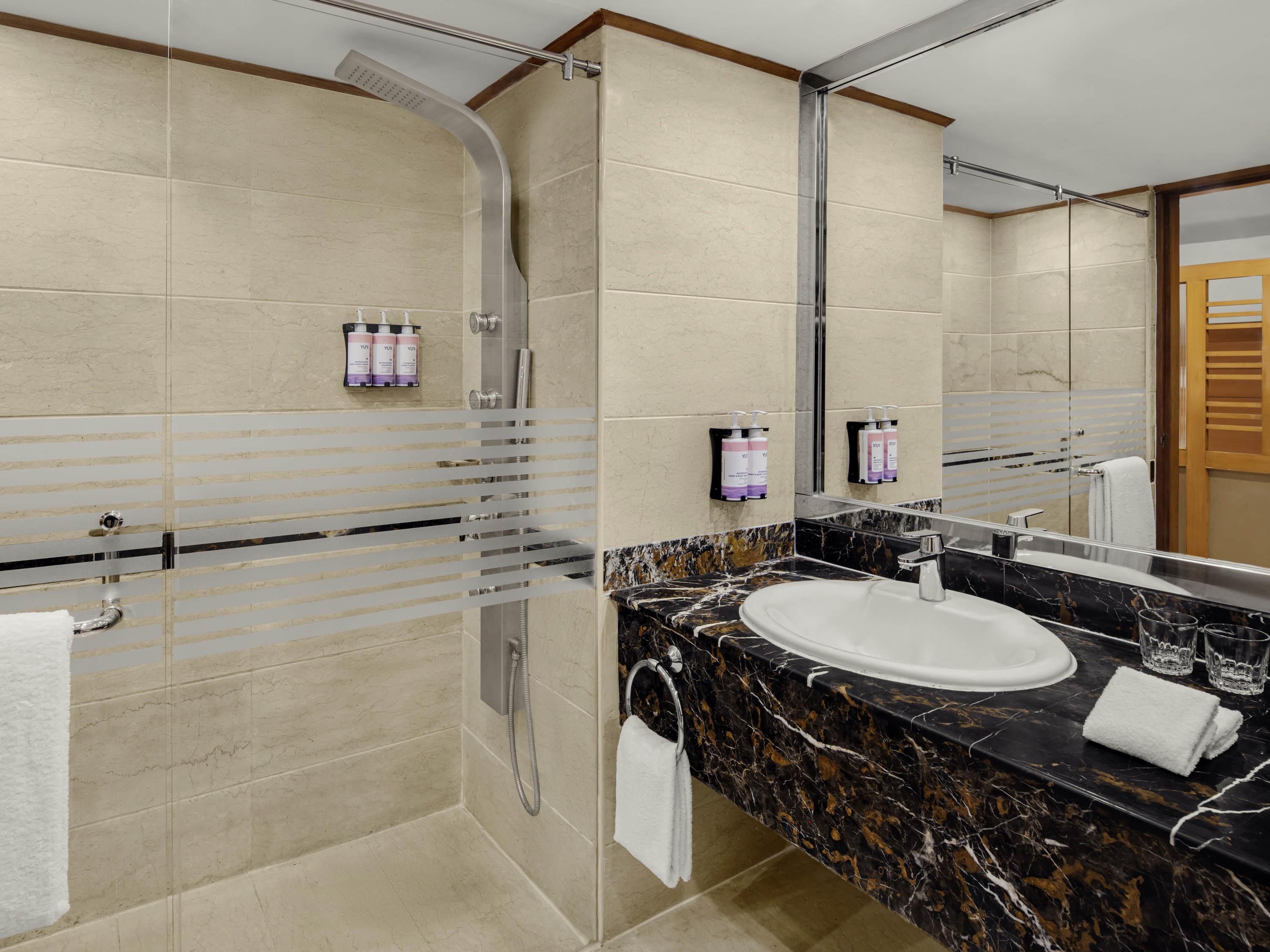 A modern bathroom with a glass-enclosed shower, a marble sink, and toiletries on the wall.