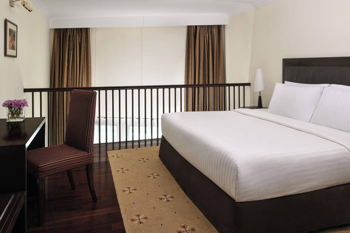 Ein Hotelzimmer mit Bett, Sessel, Schreibtisch, Lampe und Blick ins Freie.