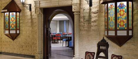 Un restaurante libanés con paredes de piedra, ventanas de vitral y una zona de estar acogedora con un tapiz decorativo.