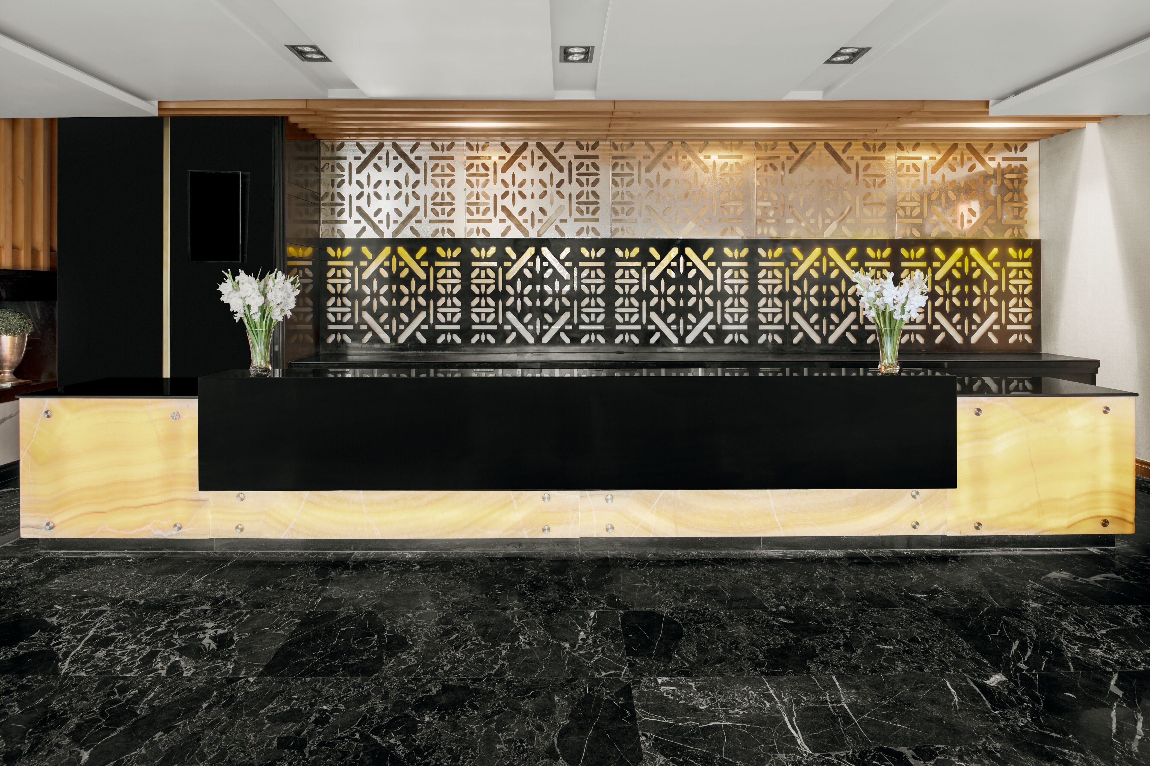 A reception desk with a black marble floor, a wooden counter, and a patterned wall.