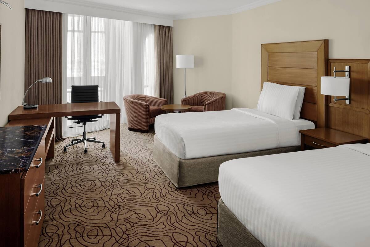 Ein Hotelzimmer mit zwei Betten, einem Schreibtisch, einem Stuhl, einer Lampe und einem Nachttisch.