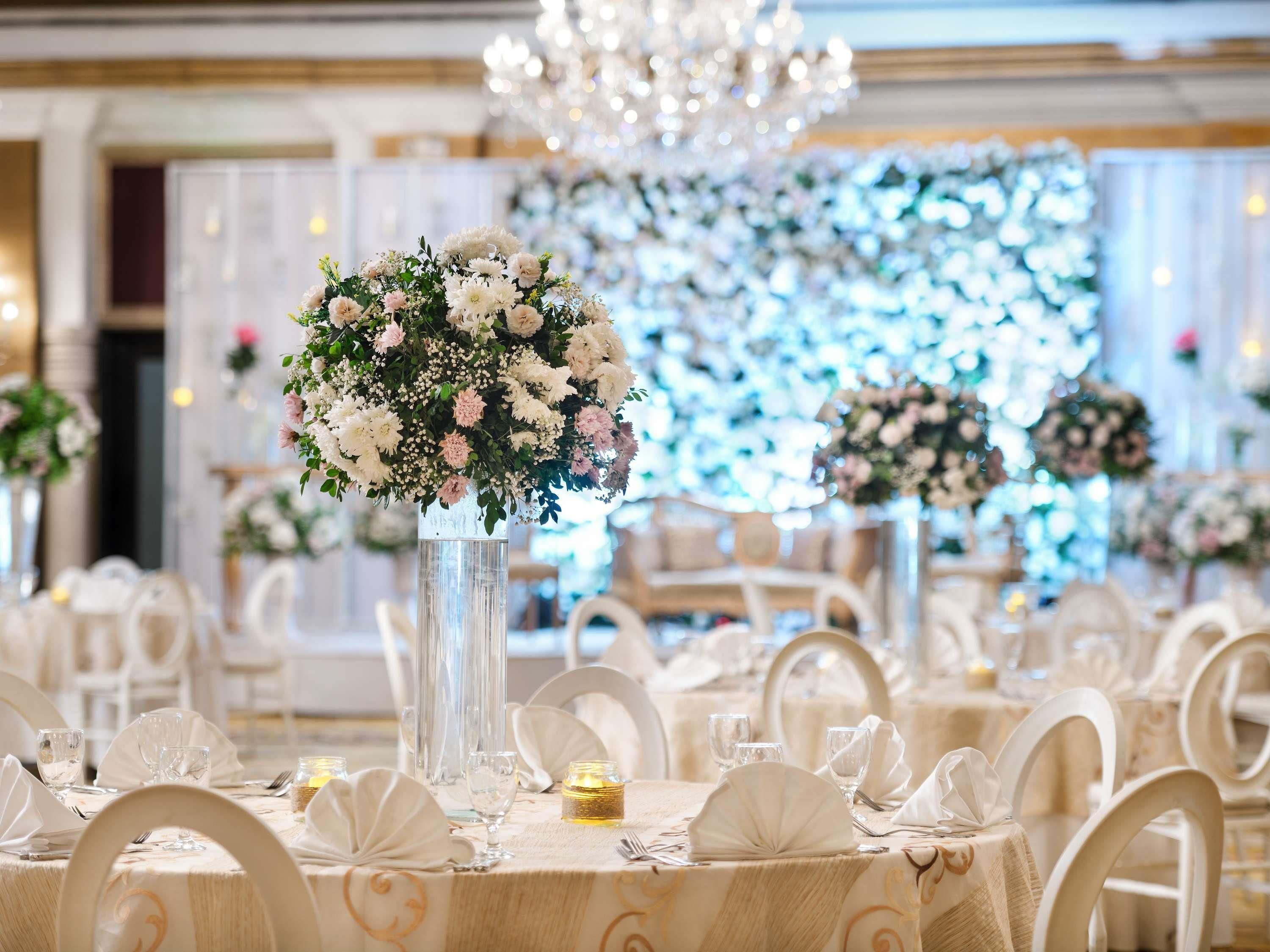 Un salón de banquetes con mesas redondas, sillas blancas y centros de mesa florales.