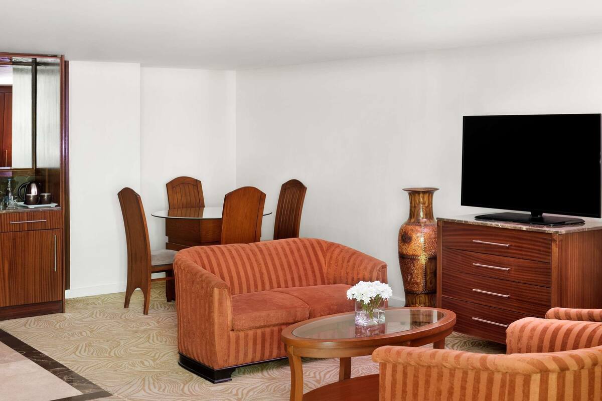 Una sala de estar con sofá, sillones, una mesa de centro, televisor, mueble de almacenamiento y una mesa de comedor con sillas.