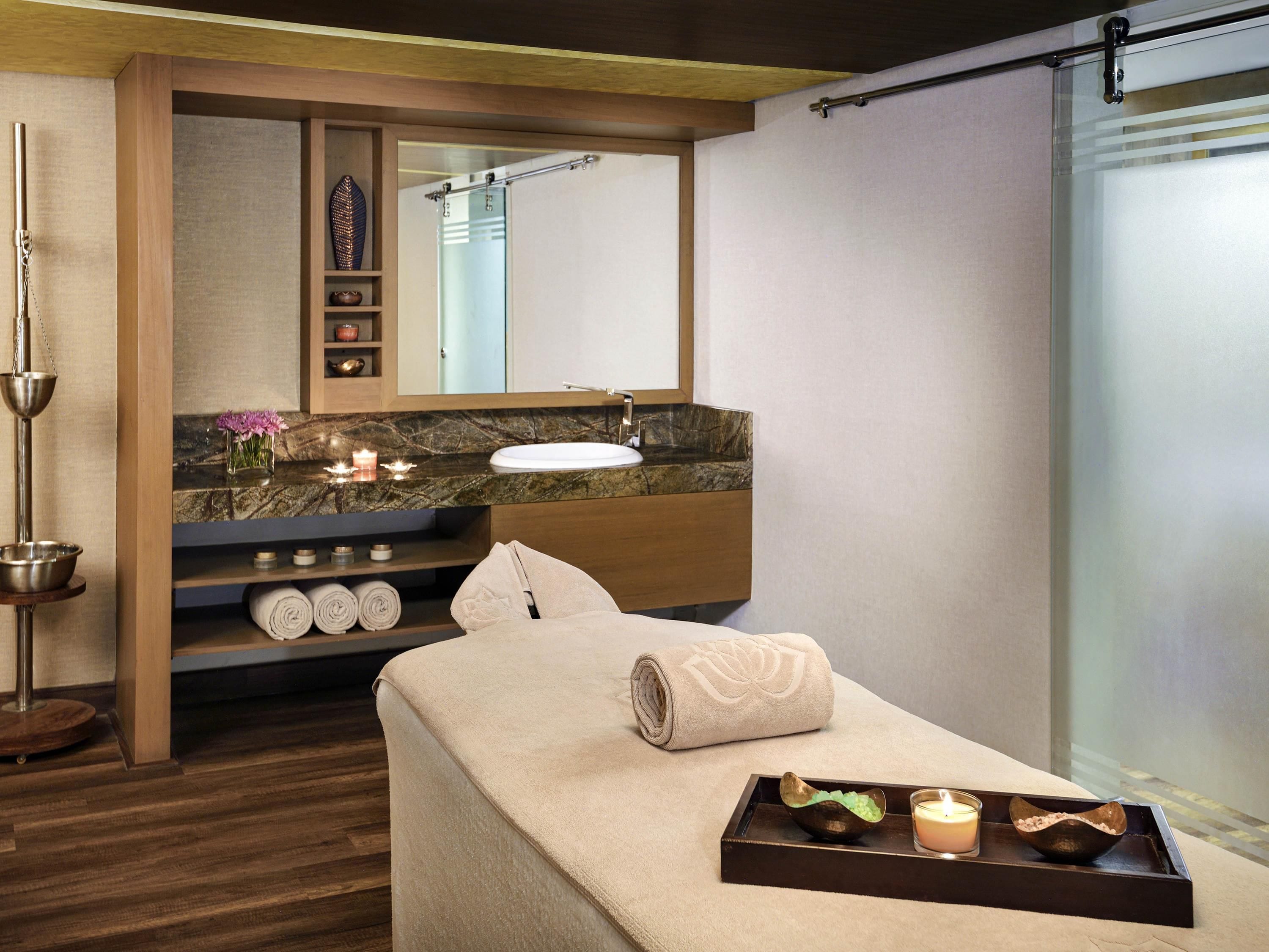A modern bathroom with a wooden vanity, a large mirror, a bathtub, and a massage table with towels and candles.