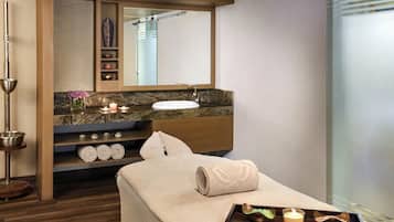 A modern bathroom with a wooden vanity, a large mirror, a bathtub, and a massage table with towels and candles.