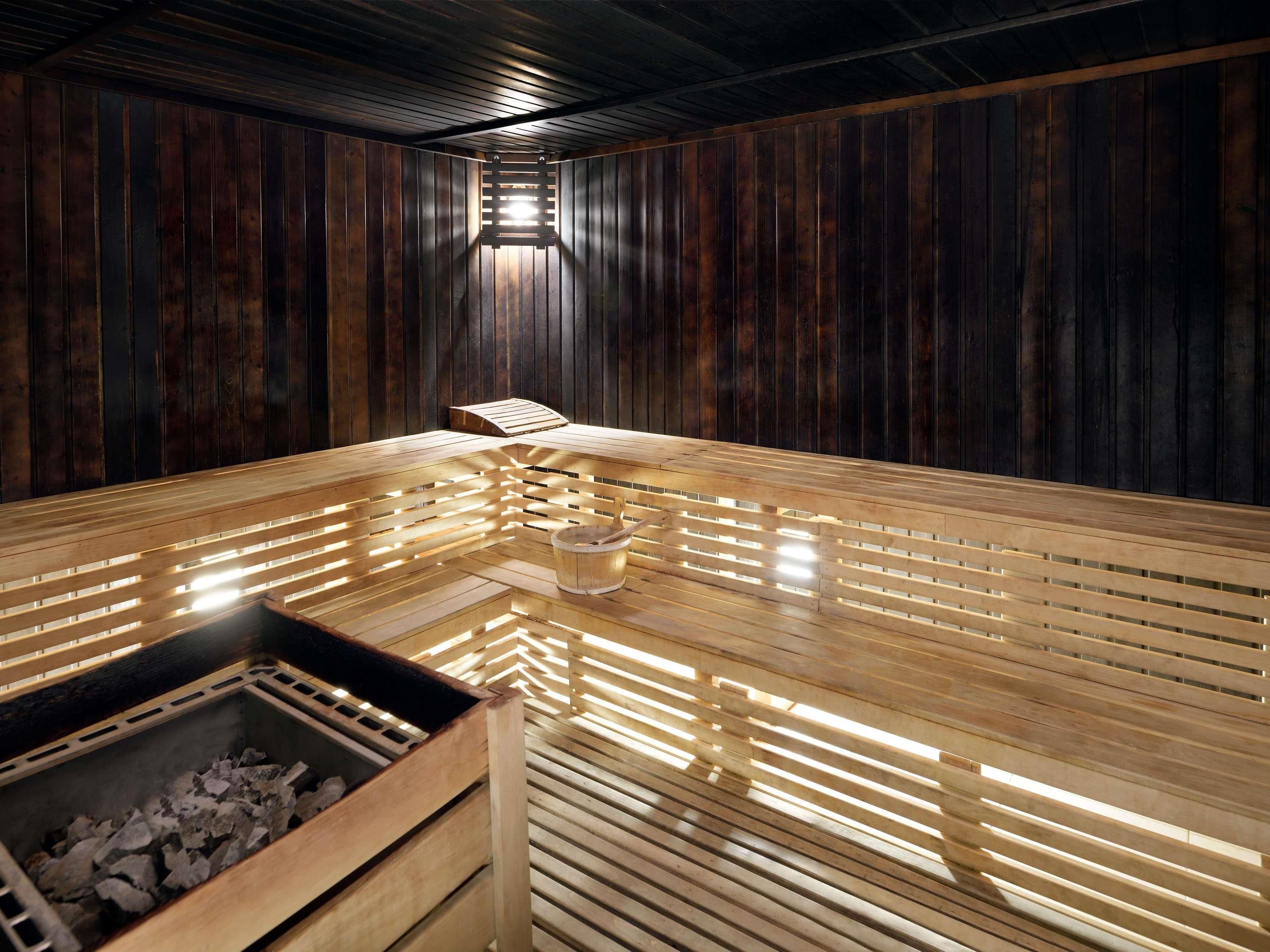 Una sauna con bancos de madera y piso de tablas, un balde y una ventana pequeña para luz natural.