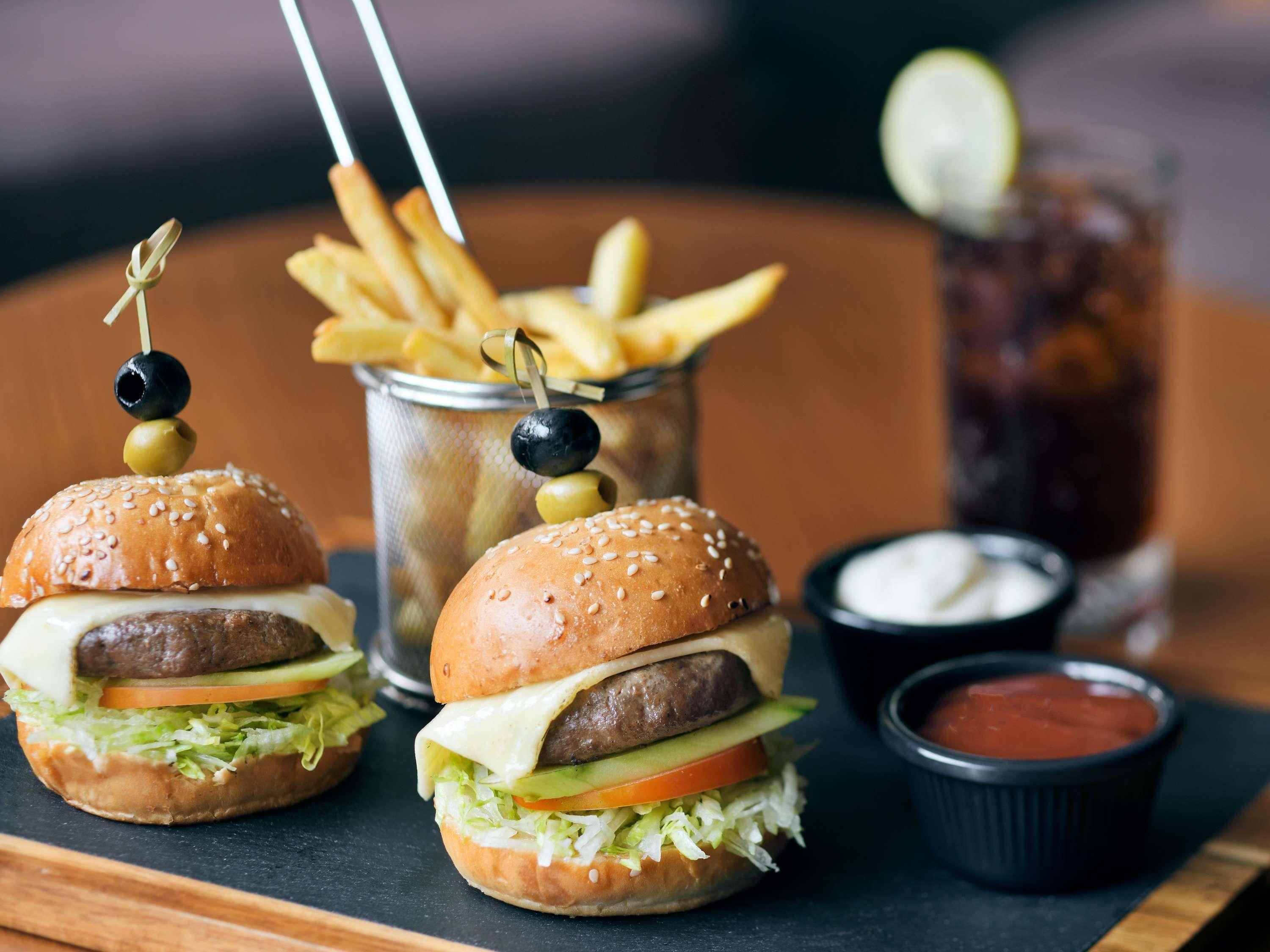 Two burgers with olives on skewers, a container of fries, and two small bowls of sauce.