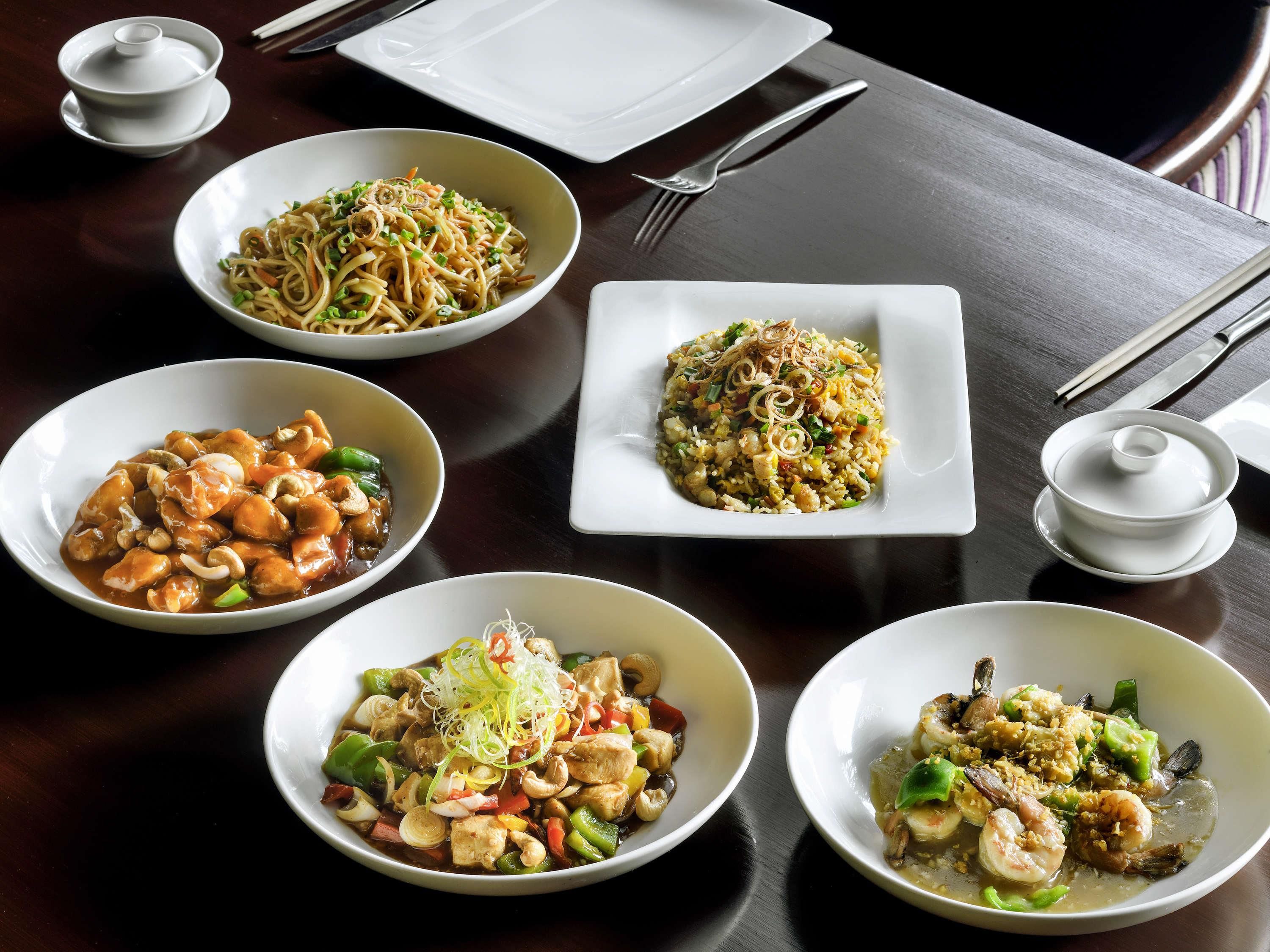 A table with various dishes, chopsticks, and a teapot.