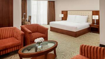 A hotel room with a large bed, two armchairs, a glass coffee table, and a view of the outside.