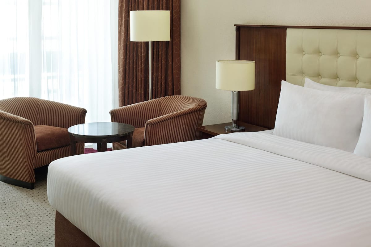 Hotellihuone, jossa on suuri sänky, kaksi nojatuolia, pieni pyöreä pöytä ja kaksi yöpöytävalaisinta.