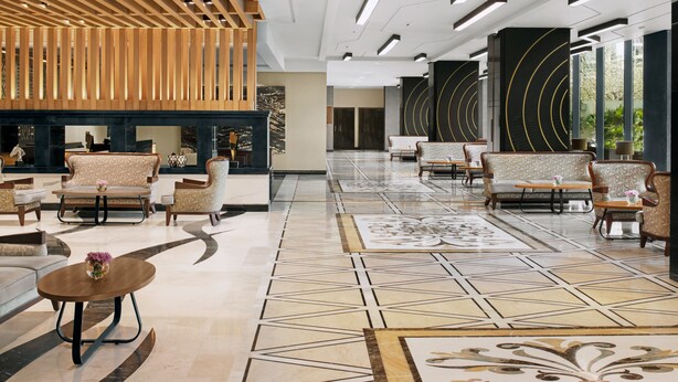 A spacious lobby with modern furniture, a patterned floor, and a wooden ceiling structure.