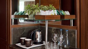 A kitchen counter with a coffee maker, cups, glasses, and a plant.