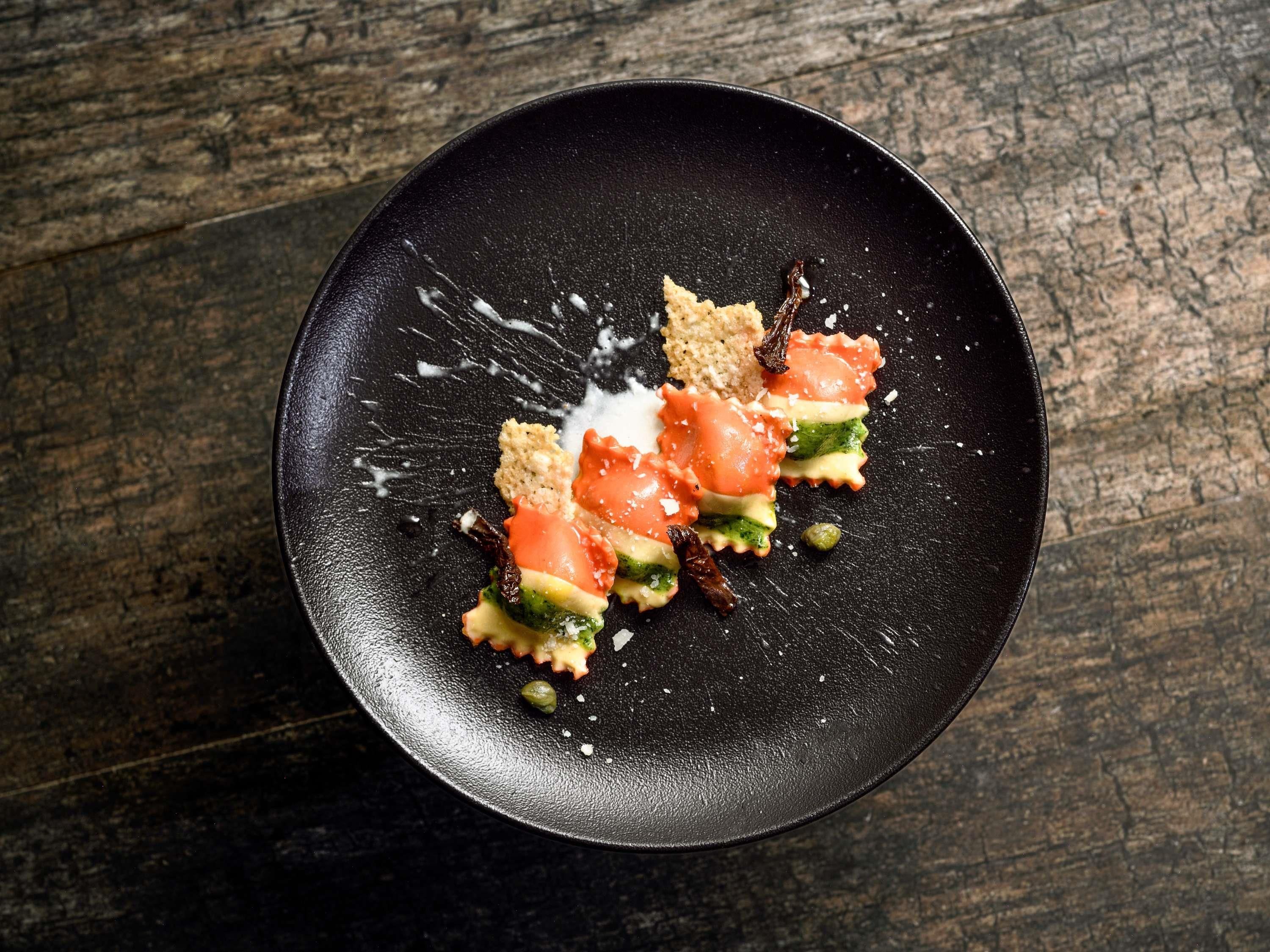 A black plate with food on a wooden surface.