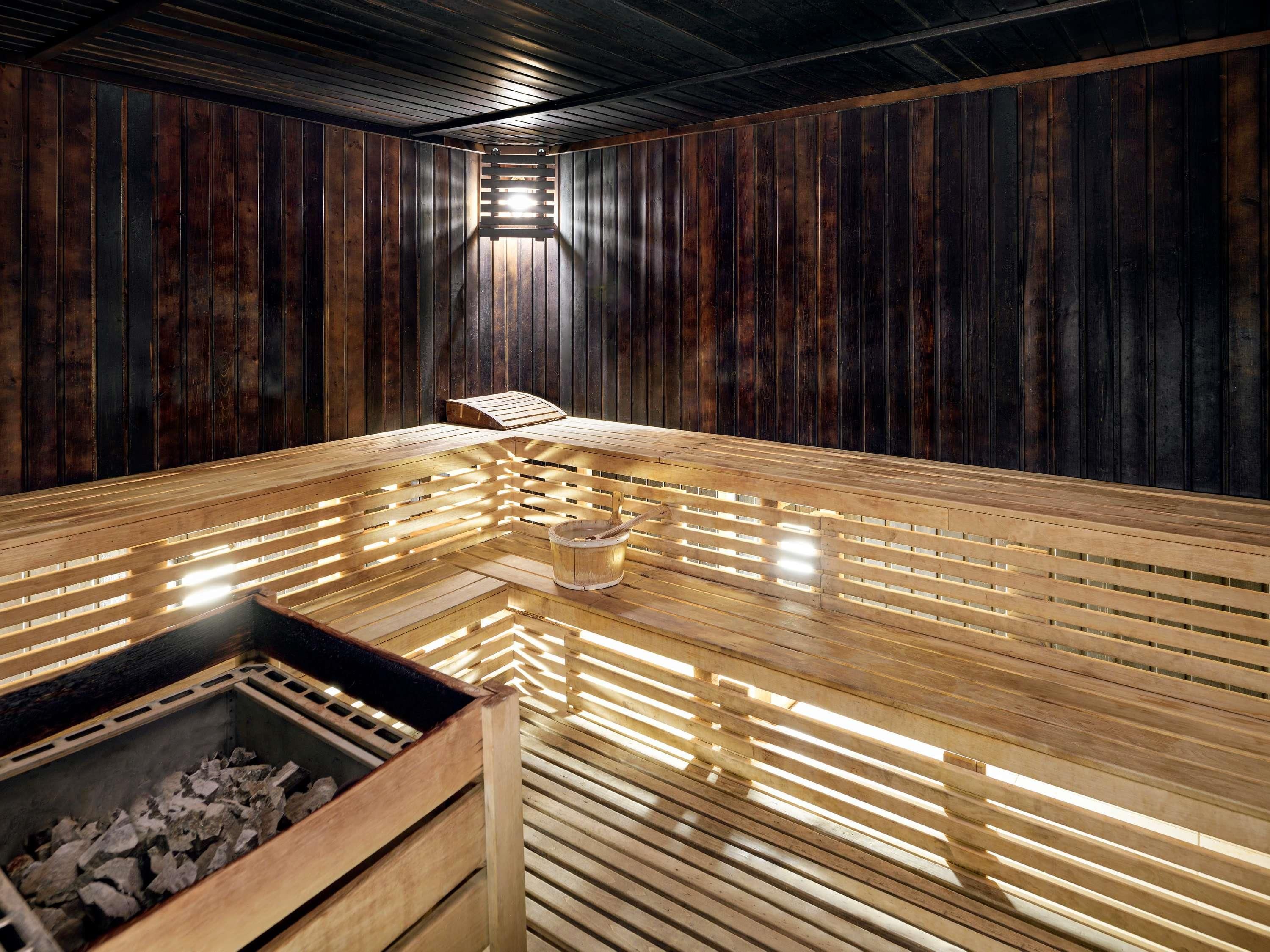 A sauna with wooden benches and a central heating element, surrounded by dark wooden walls.