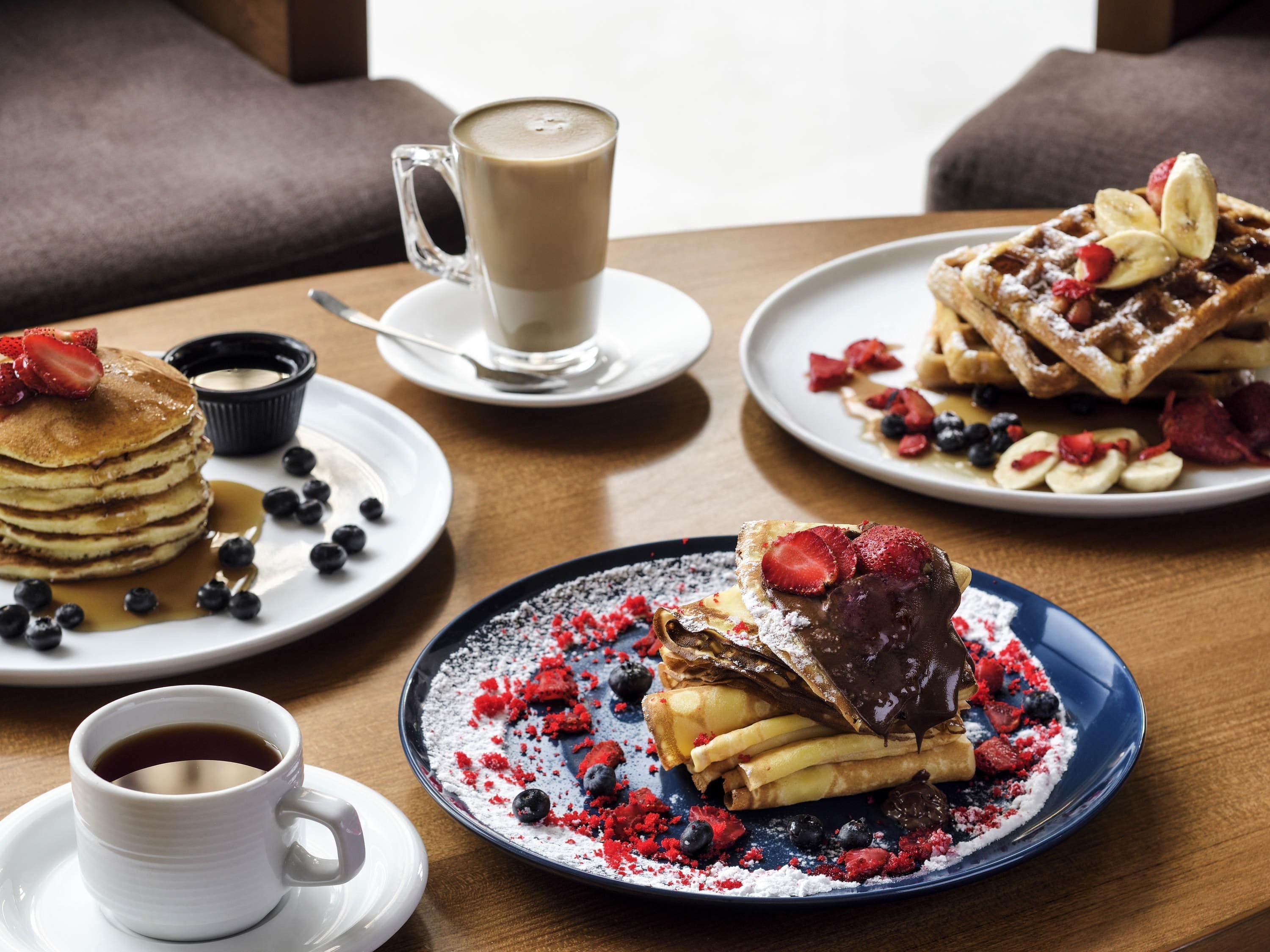 Desayuno con tortitas, gofres y una taza de café sobre una mesa.