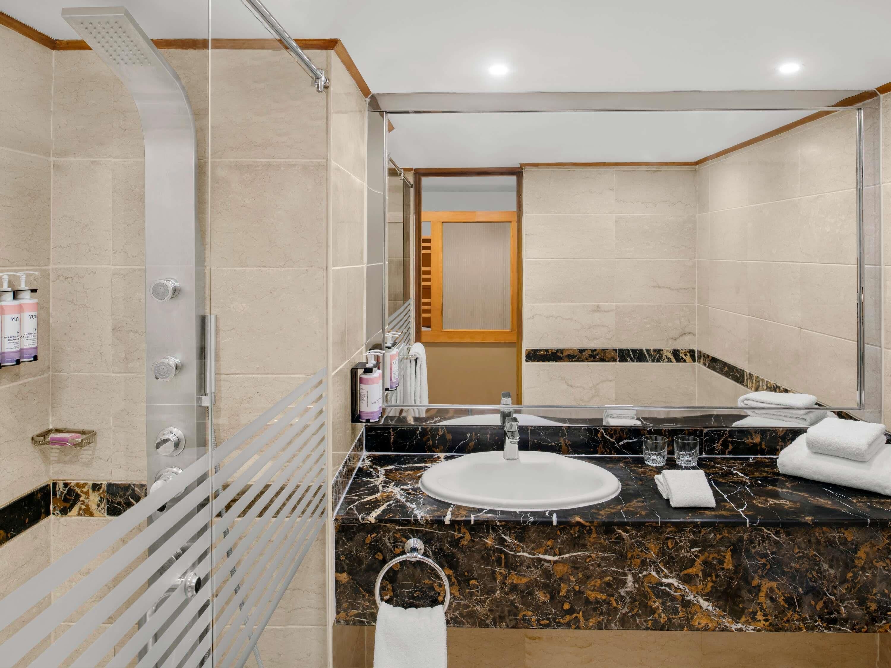 Un baño moderno con ducha envuelta en vidrio, lavamanos de mármol y un espejo grande.
