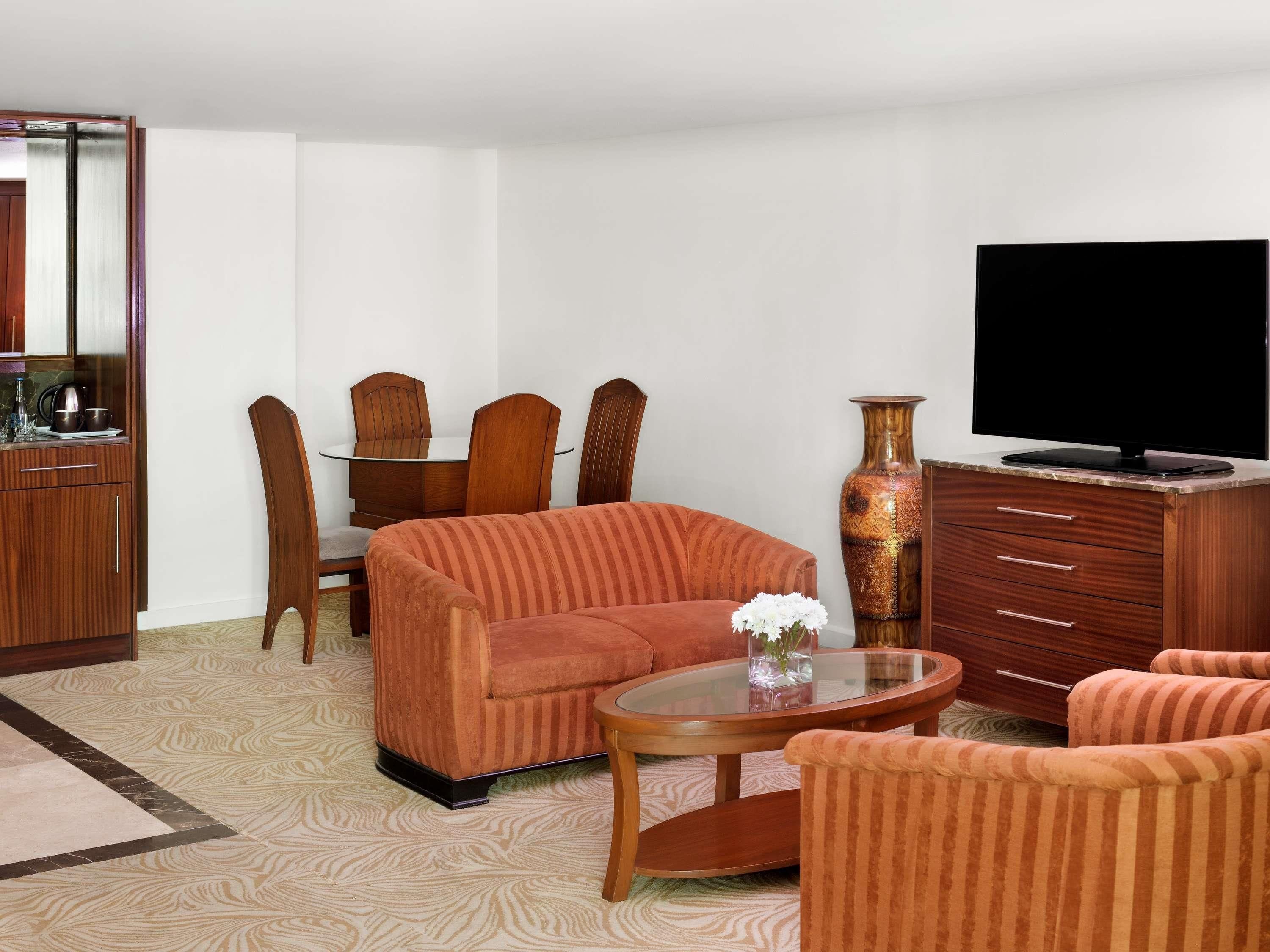 A living room with a sofa, armchairs, a coffee table, a TV, a cabinet, and a dining table with chairs.