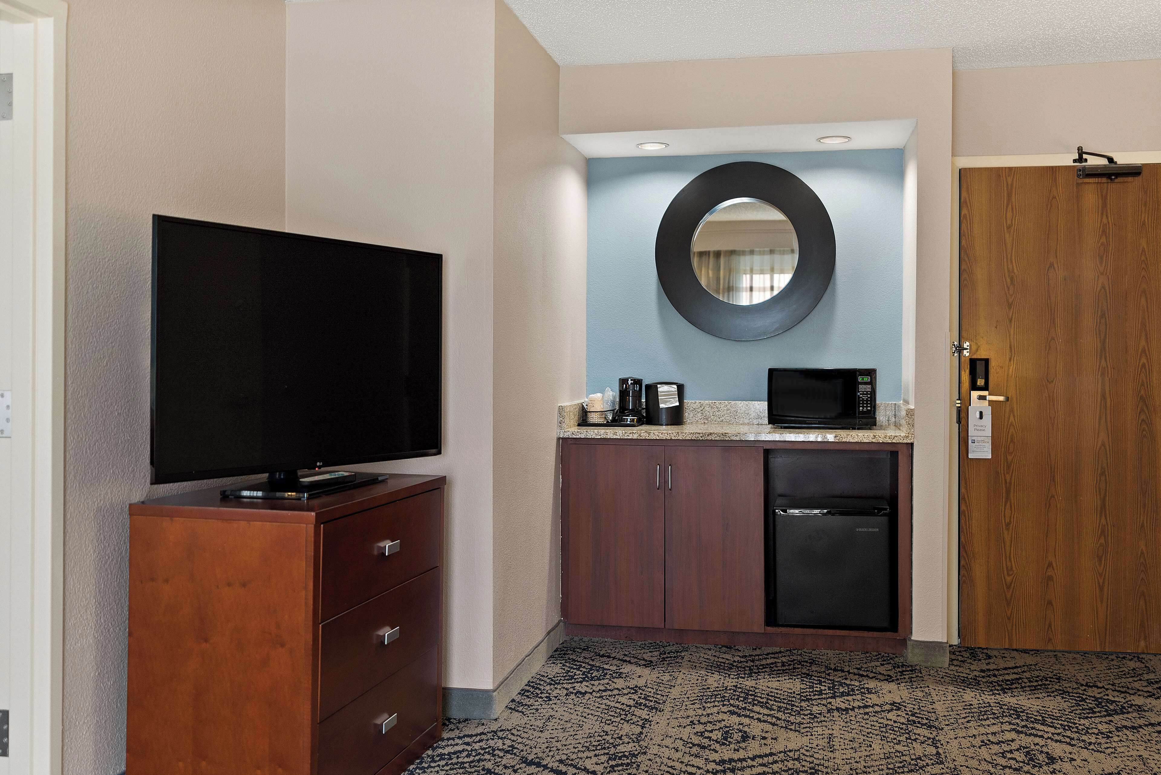 A hotel room with a flat-screen TV, a microwave, a coffee maker, a refrigerator, and a wooden door.