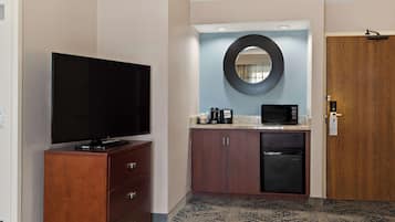 A hotel room with a flat-screen TV, a microwave, a coffee maker, a refrigerator, and a wooden door.