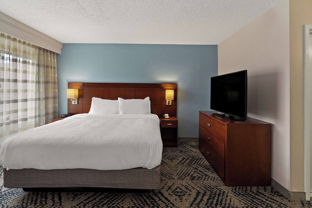 Una camera d'albergo con un letto grande, una televisione su un comò in legno e un comodino con una lampada.