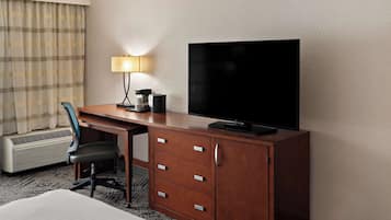 A hotel room with a wooden desk, a television, a lamp, a chair, and a bed.