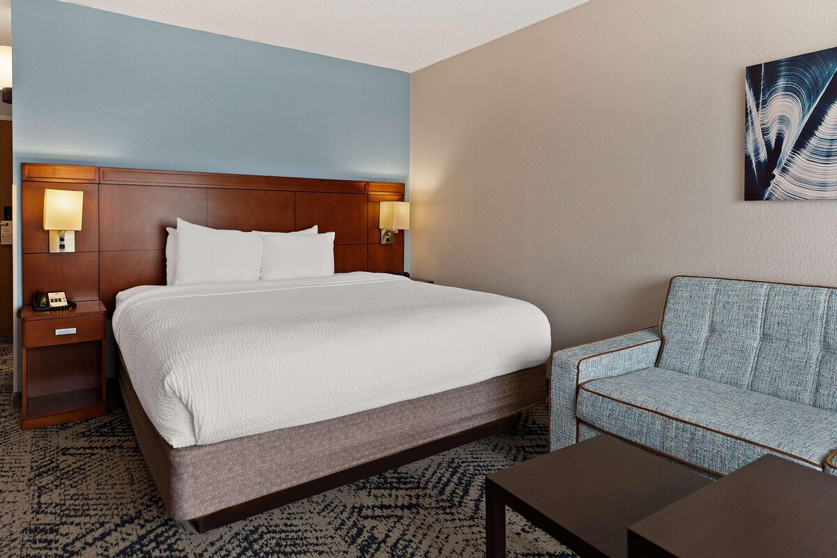 A hotel room with a bed, bedside tables, a sofa, and a painting on the wall.