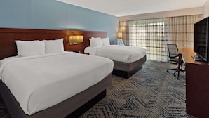 A hotel room with two beds, a desk, a TV, and a window with curtains.