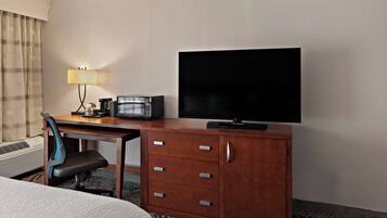 A hotel room with a wooden desk, a television, a lamp, and a chair.