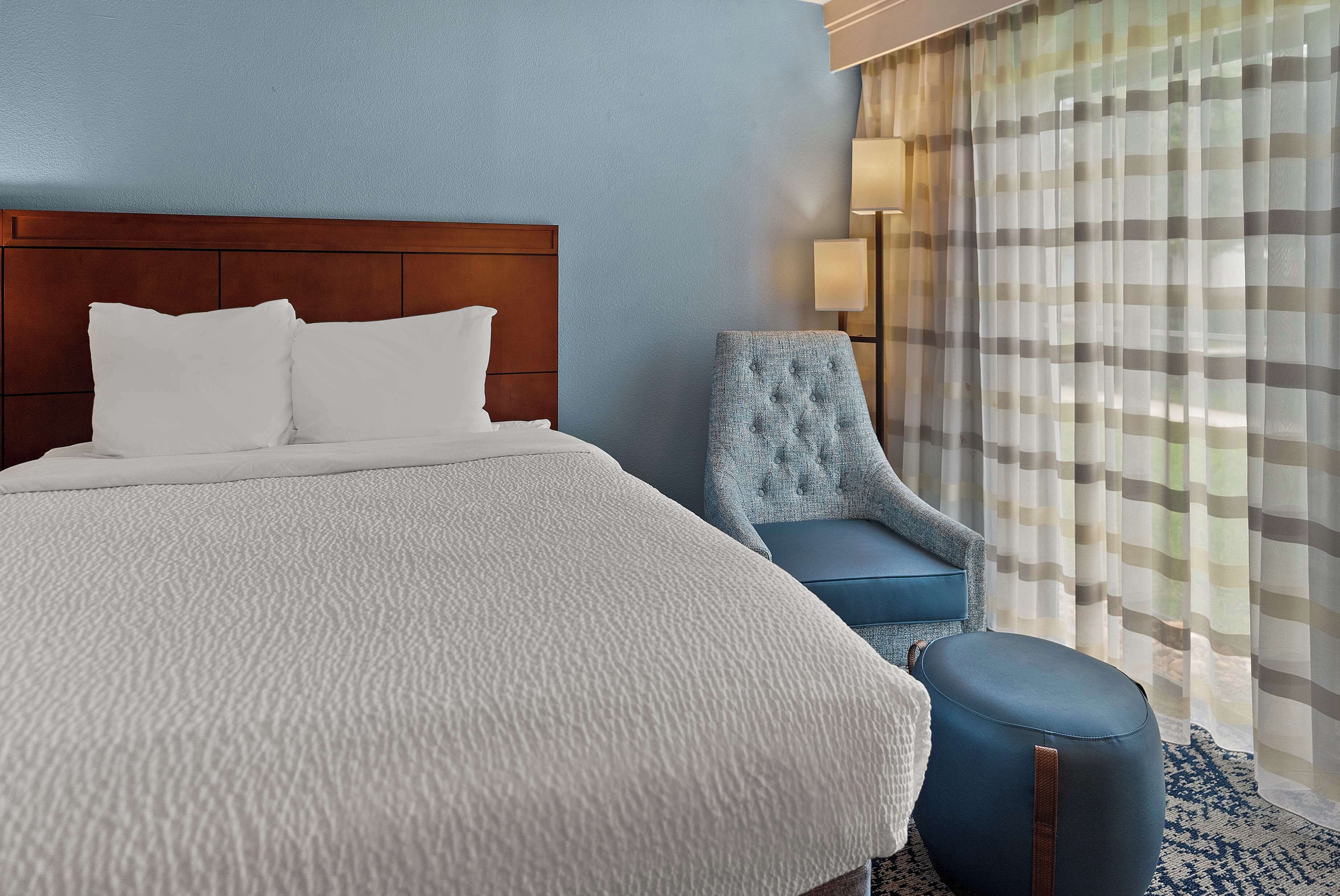 A hotel room with a large bed, a blue armchair, and a small ottoman.