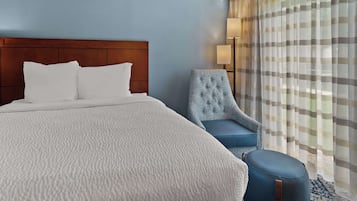 A hotel room with a large bed, a blue armchair, and a small ottoman.