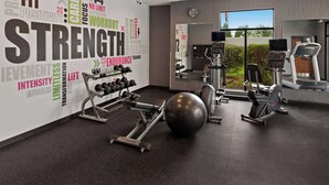 A modern gym with various exercise equipment, motivational wall graphics, and a large window offering a view of the outdoors.