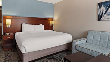 A hotel room with a large bed, a nightstand with a lamp, a sofa, and a painting on the wall.