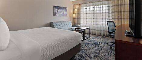A hotel room with a large bed, a desk, a chair, a television, and a window with curtains.