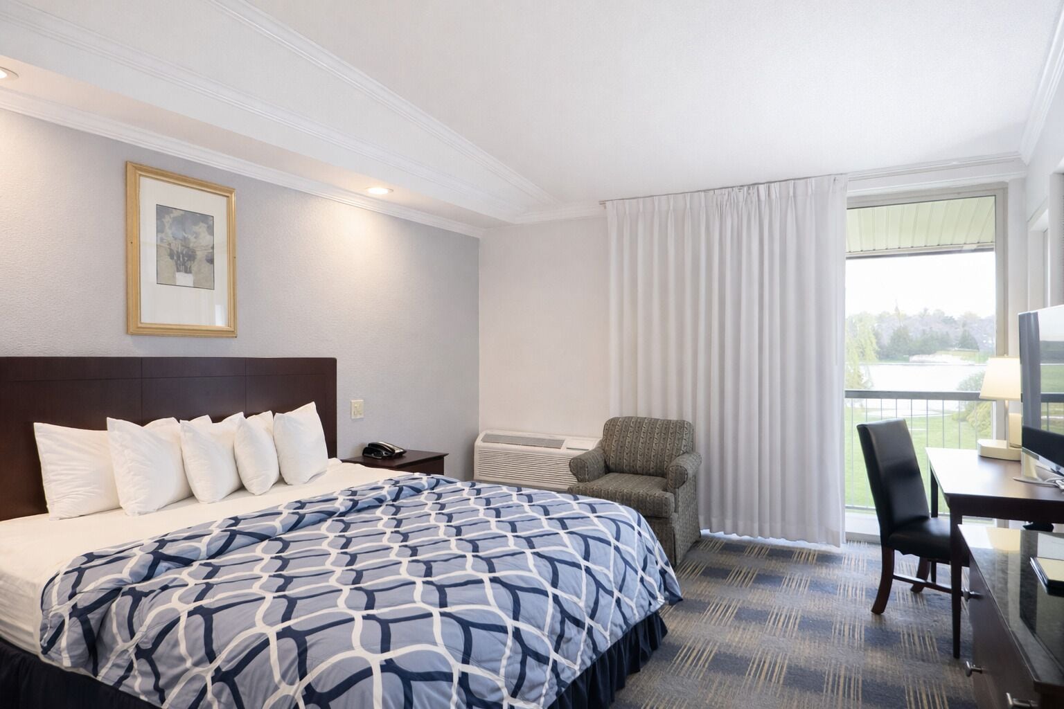 Una camera d'albergo con un letto grande, una scrivania con una sedia, una televisione e una finestra con tende.