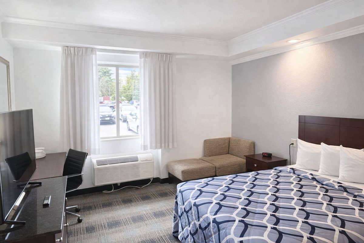 A hotel room with a bed, a desk with a chair, a TV, and a window with curtains.