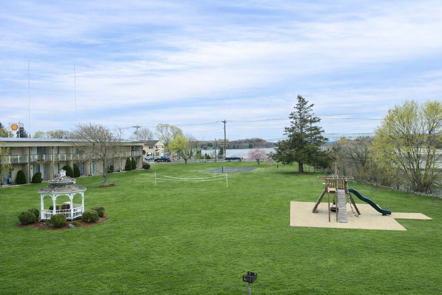 A grassy yard with a gazebo, a playground with a slide, and a building with a balcony in the background.