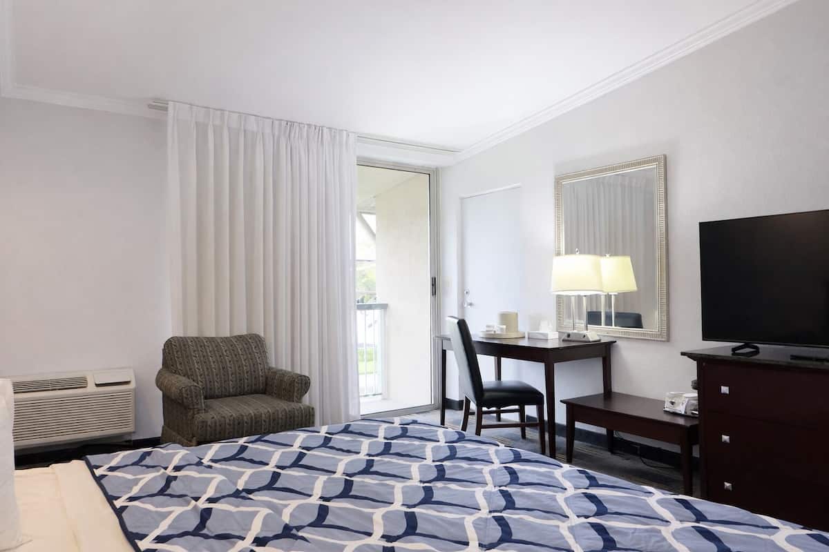 A hotel room with a bed, a desk with a chair, a television, and a window with curtains.