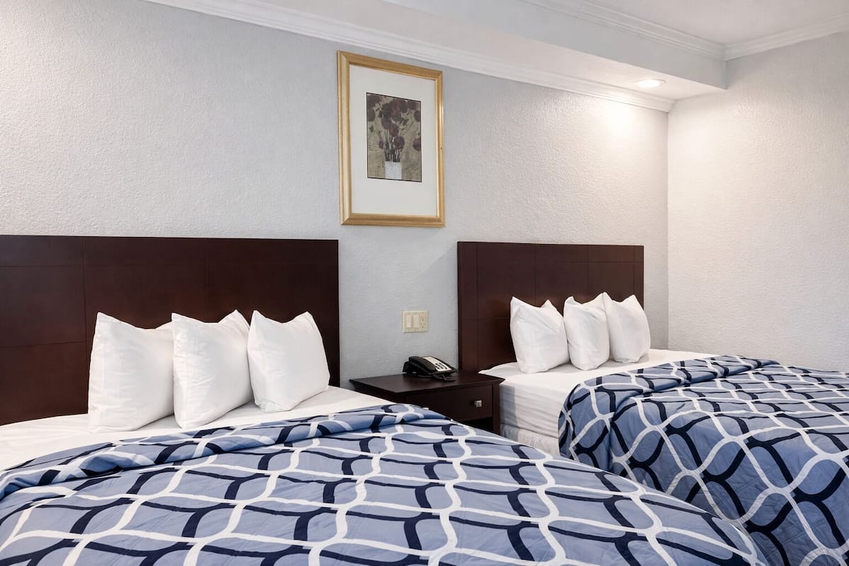 A hotel room with two beds, a nightstand, a phone, and a framed picture on the wall.