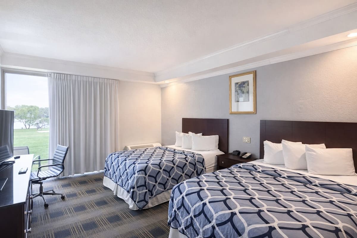 A hotel room with two beds, a desk, a chair, and a large window with curtains.