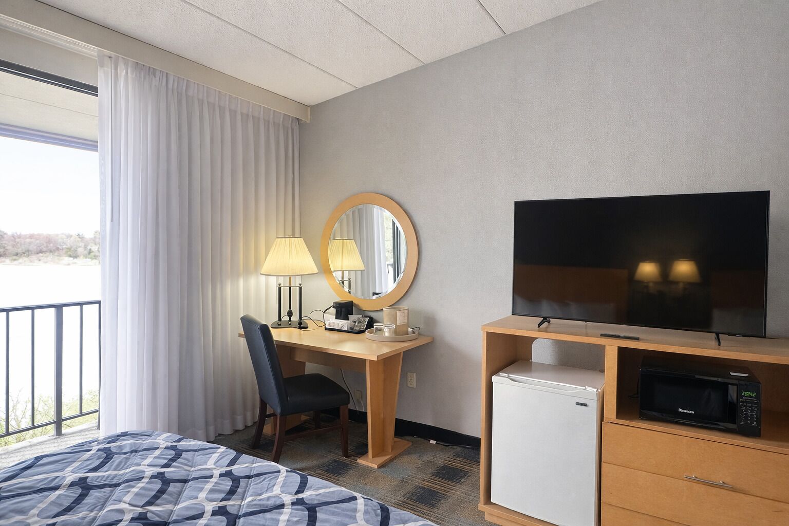 Una habitación de hotel con cama, escritorio con silla, televisor, microondas y ventana con cortinas.