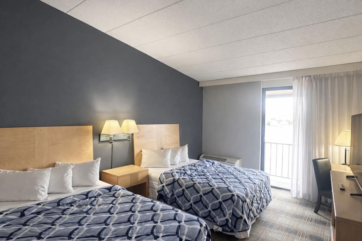 A hotel room with two beds, a desk, a chair, a lamp, and a window with curtains.