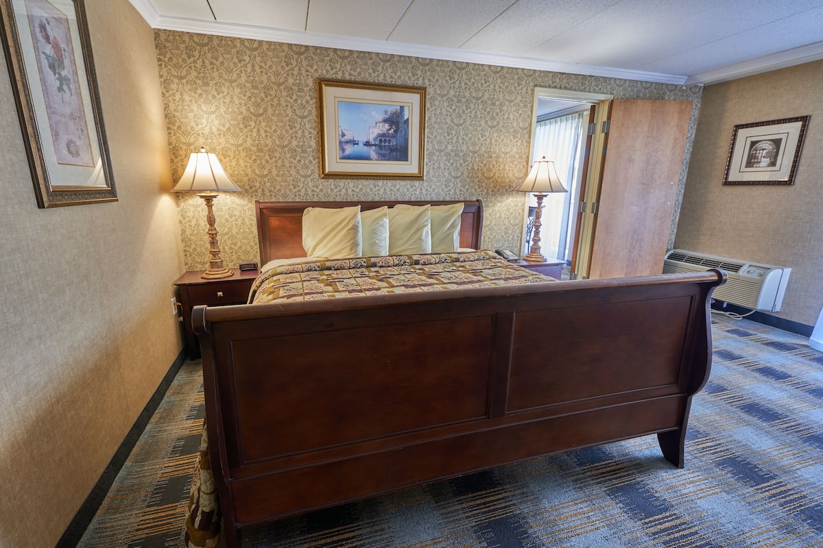 A hotel room with a large bed, two bedside tables, a nightstand, a wall-mounted lamp, and a framed picture above the bed.