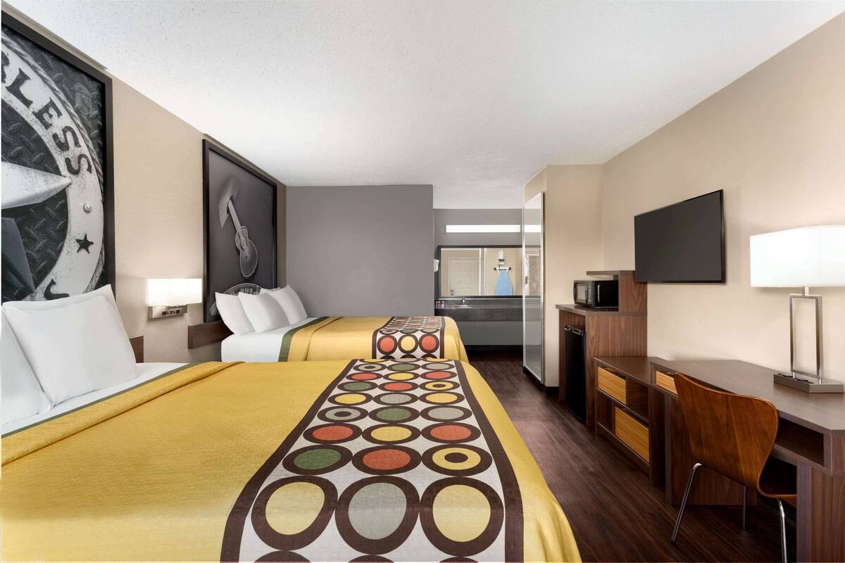 A hotel room with two beds, a desk, a TV, and a mirror.