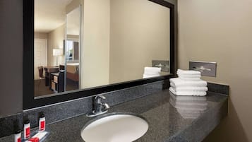 Un baño de hotel con encimera de granito, lavabo blanco y un espejo grande.