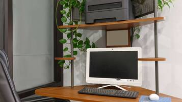 Un escritorio de computadora con monitor, teclado y ratón. Una impresora se encuentra sobre una estantería encima del escritorio.