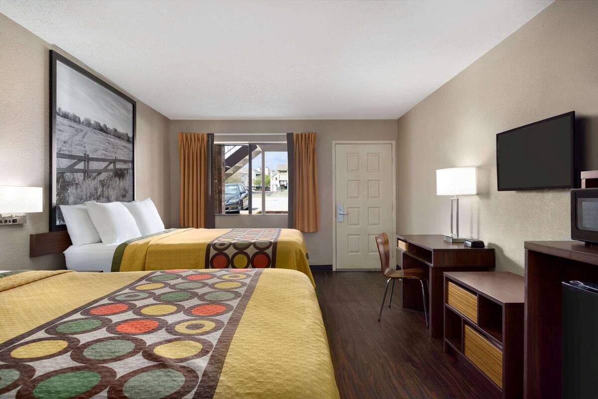 A hotel room with two beds, a desk, a chair, a television, and a window with curtains.