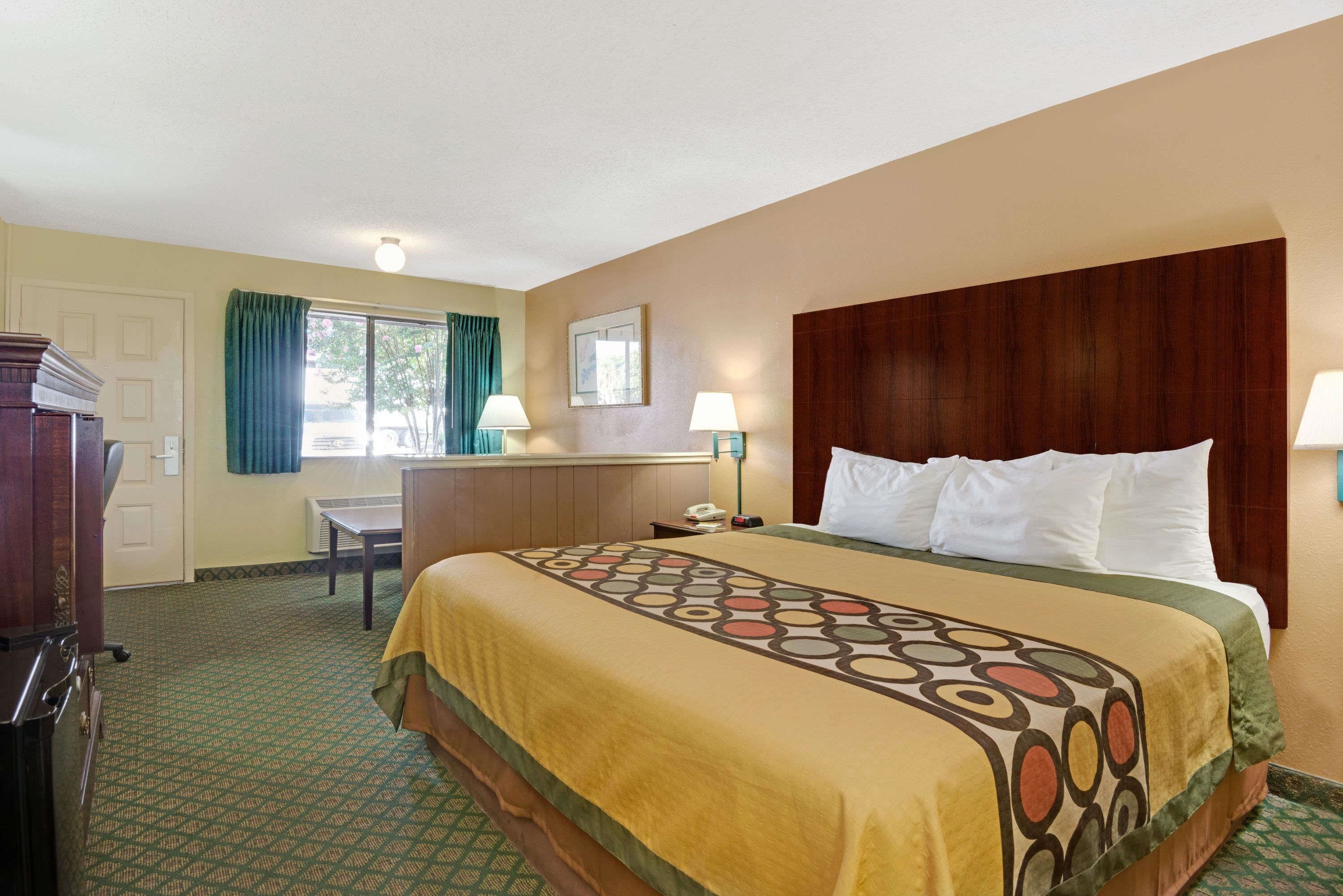 A hotel room with a large bed, a desk, a chair, and a window with curtains.