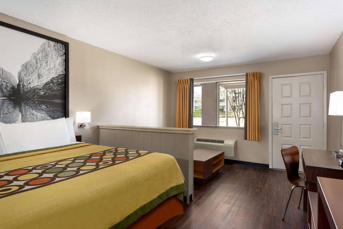A hotel room with a bed, a desk, a chair, a window with curtains, and a door.