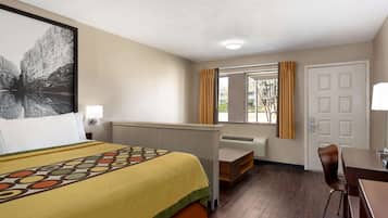 Une chambre d’hôtel avec un lit, un bureau, une chaise, une fenêtre avec des rideaux et une porte.